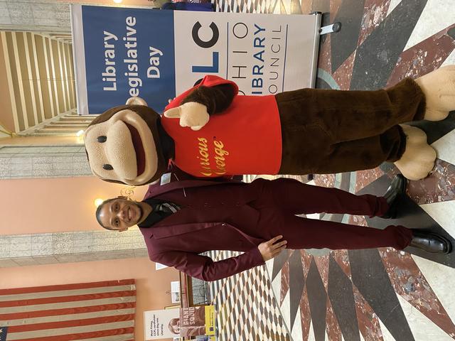 a young Black man with a curious george mascot during library legislative day for the ohio library council