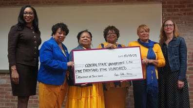 six people smile at the camera while four of them hold a large check during a ceremony honoring the late Mit Joyner, former NASW president, at Central State University