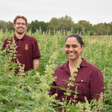Two people wearing Central State University maroon and gold smile at the camera while standing in a field of green crops