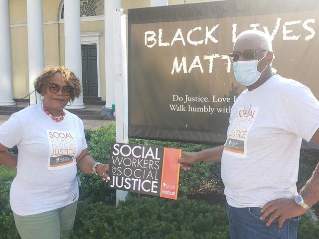 two individuals including Mit Joyner hold a sign that says Social Workers Social Justice in front of a Black Lives Matter sign