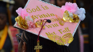 a student customizes her cap to read "God is within her, she will not fall" from Psalms 46:5
