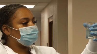 A young Black environmental engineer, Jasmine Walker, wearing a white lab coat and blue protective gloves holding a test tube for water quality testing