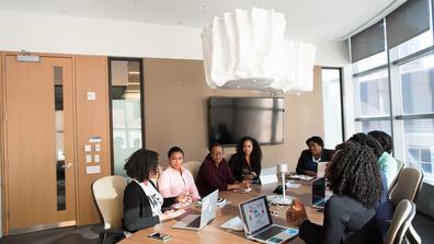 Eight professionals collaborate around a conference table in a workplace