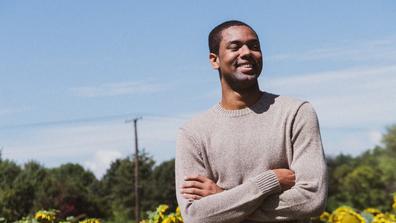 Black man crossing his arms and smiling in a field of sunflowers