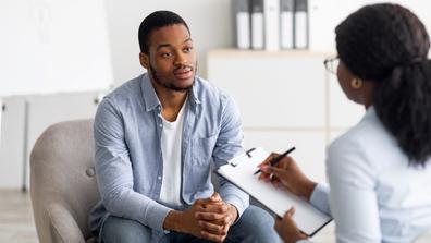 a behavioral health worker takes notes while speaking to a young Black man in an office setting