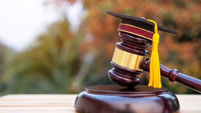 A judge's gavel with a tiny graduation cap on top