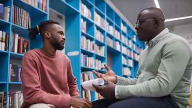 an African American student sits with an advisory in a library to discuss classes and academic progress