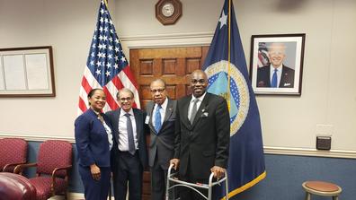 four people stand in front of a U.S. flag in a conference room