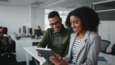 Smiling young african american professional businessman and businesswoman together working online with a digital tablet in office