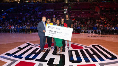 six people stand on a basketball court holding a large check presented to nicole holt as the 2024 ohio education association aspiring educator at central state university