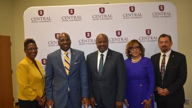 a group of people including united states department of agriculture chief terry crosby stand in front of a large central state university backdrop