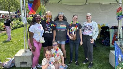 seven people of all ages under a tent with a progress pride flag flying at cleveland pride