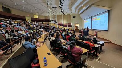 Students sit in a lecture hall; register for the event