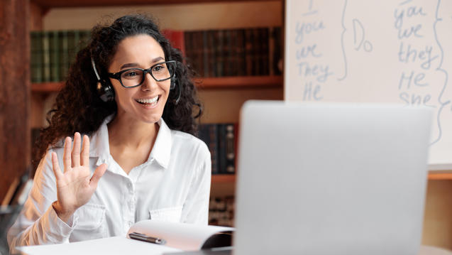 Woman with headset waving at laptop screen