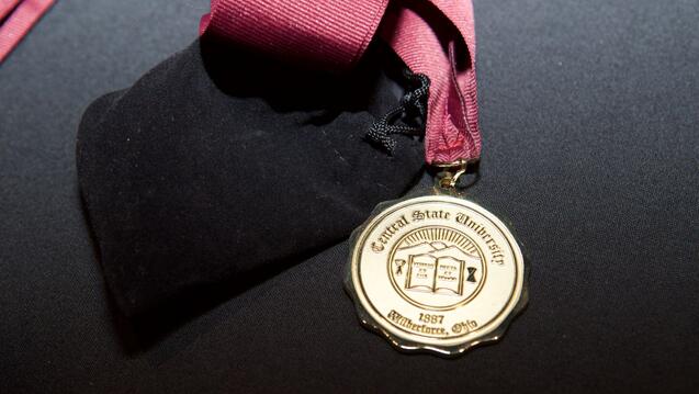 a gold medallion with the Central State University seal on a maroon landlord