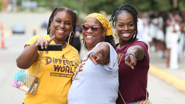 three Central State University students wearing maroon and gold point at the camera with big smiles