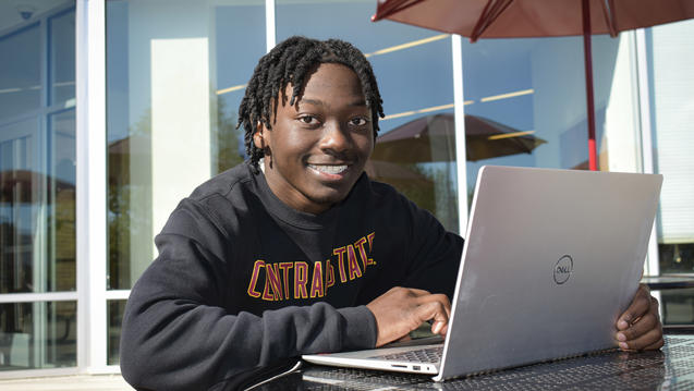 a Central State University student sitting outside the University Center with a laptop