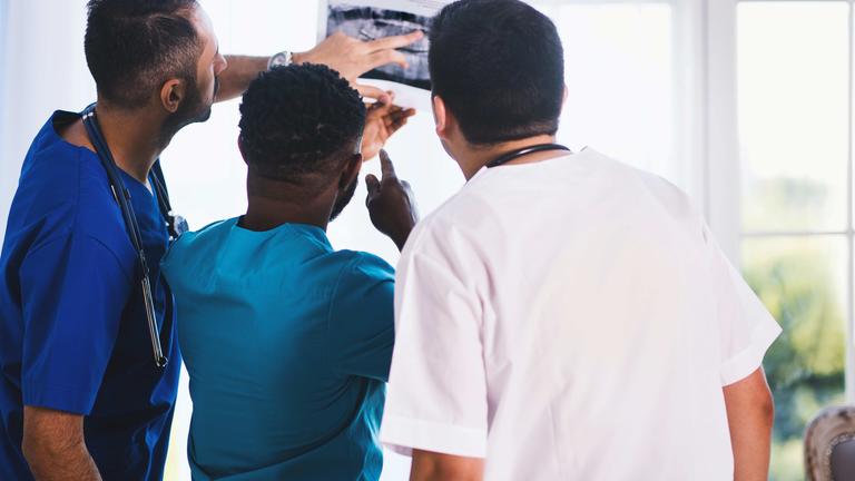 three medical professionals look at a medical device