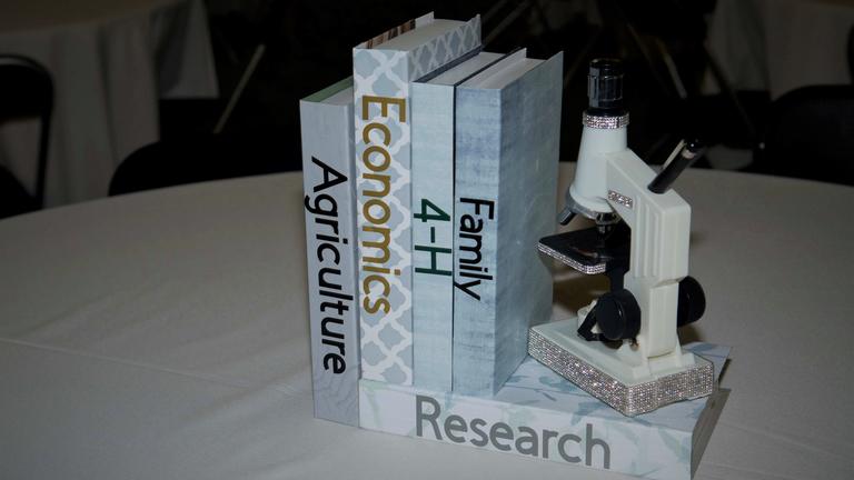 A table decoration includes a microscope and books with the words "agriculture," "economics," "4-H," "family," and "research" on the spines.