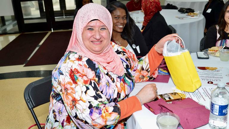 a person wearing a hajib smiles at the camera while sitting at a table