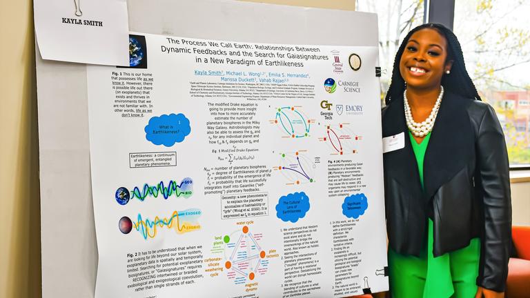 a black student stands beside a poster explaining her research at central state university