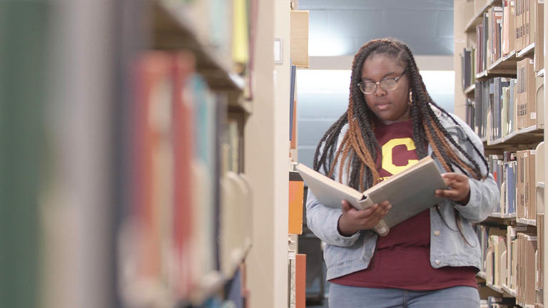 a female student with locs reads a book in between library stacks at the Hallie Q. Brown Memorial Library at Central State University