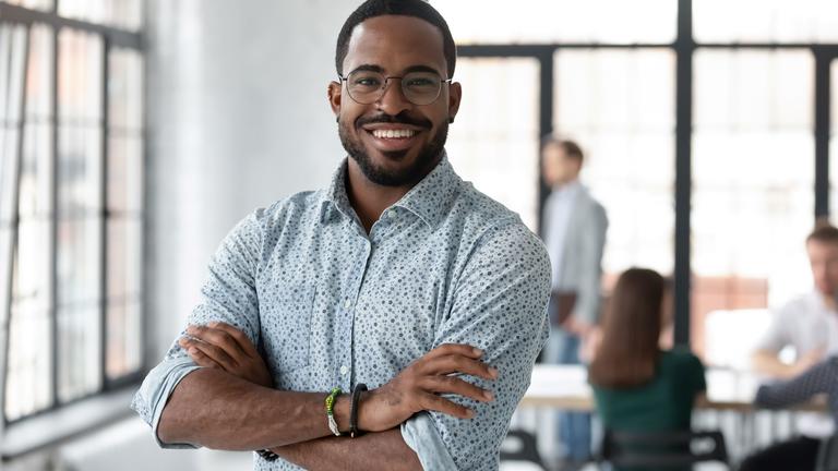 Black small business owner in a button-down shirt with arms crossed in an office setting