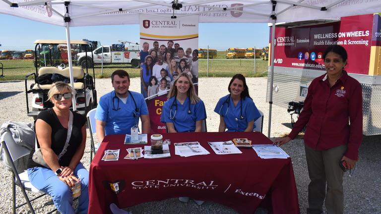 four people sit at a table under a tent at the 2023 Farm Science Review with Central State University Extension's Dr. Anshiya Ramanitharan