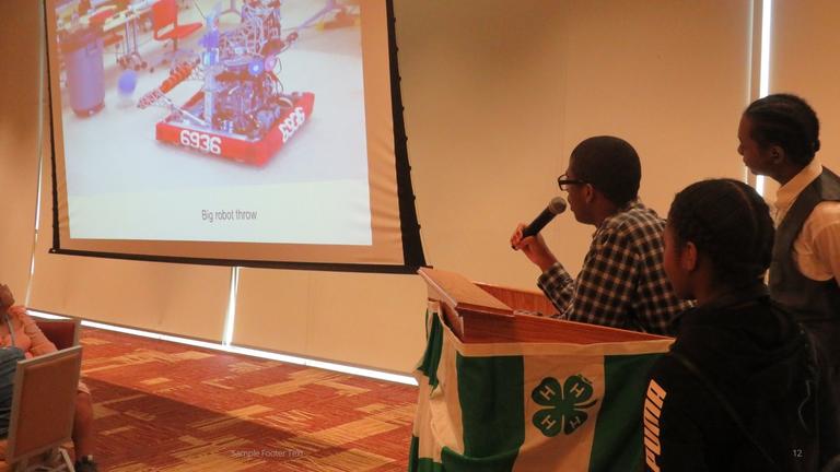 three student presenters look toward a projected photo of a robotics project during STEM camps for Dayton area youth