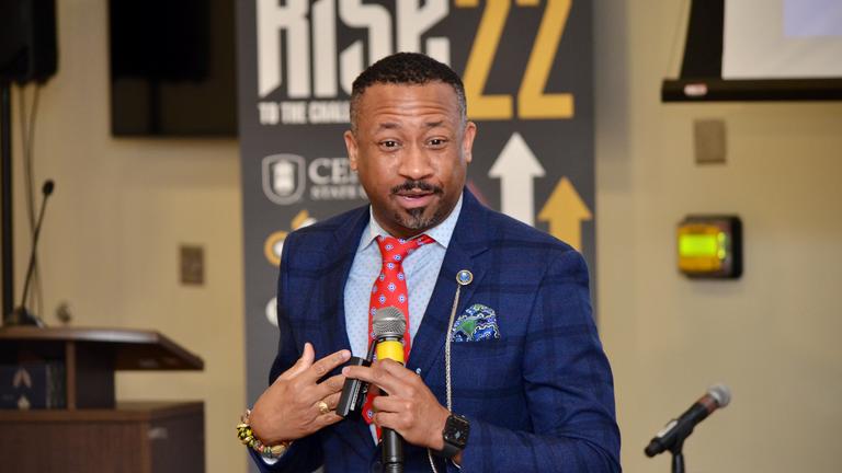 an African American speaker wearing a dark blue suit and red tie at Central State's RISE to the Challenge Summit