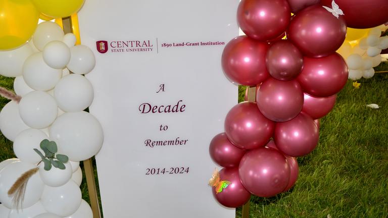 a sign with the words a decade to remember surrounded by maroon gold and white balloons