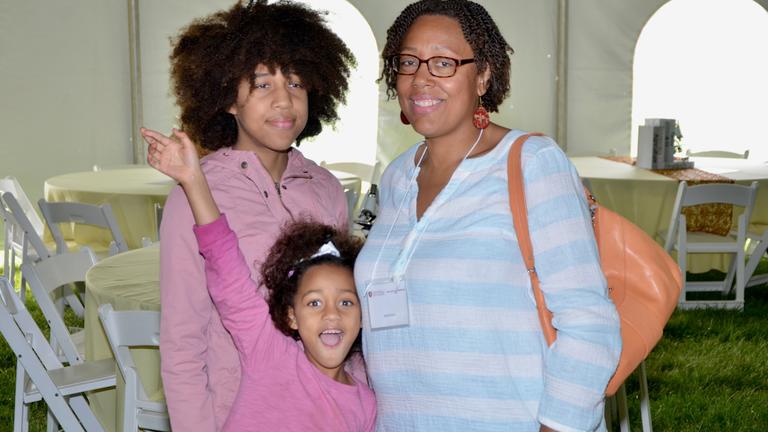 a small child raises their hand in celebration while standing with another young person and parent