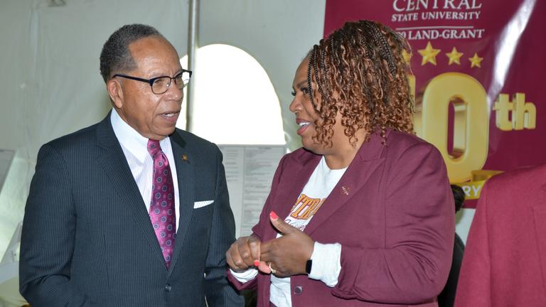 a man in a suit talking to a woman with curly hair wearing a maroon jacket