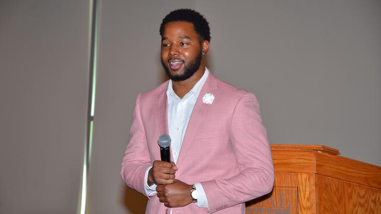 an african american man in a pink suit and white shirt holding a microphone