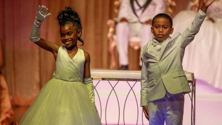 two young children wave to the crowd from a stage