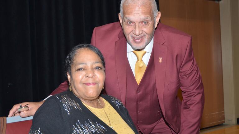 a man in a maroon shirt bends over beside a woman in a gold blouse and black sweater