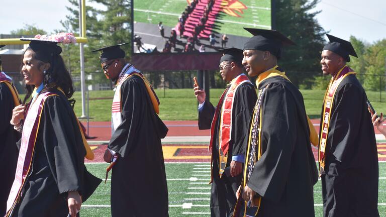 graduates on the field with an aerial view on the jumbotron