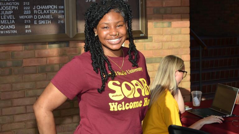 a young person smiles at the camera wearing a maroon and gold shirt