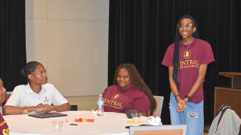 two students sitting at a table while another stands