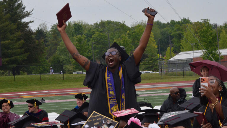 a student raises their diploma above their head in celebration