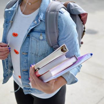 A college student with purple nail polish carries a set of books while weaing a backpack
