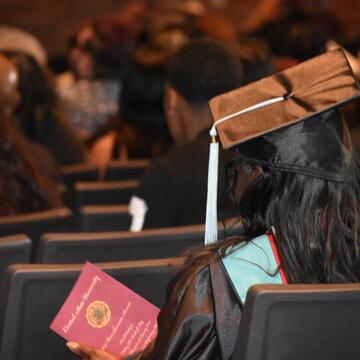 the back of a graduate wearing a cap and tassel in an auditorium