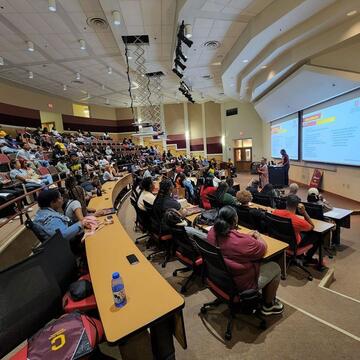 Students sit in a lecture hall; register for the event
