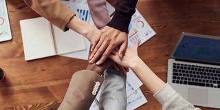 diverse people stack hands together with workplace paperwork and a laptop in the background representing central state university center of excellence hbcu corporate engagement partnerships