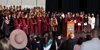 president thomas (center) stands on stage with participants of the 2023 charter day convocation