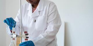 A Black scientist works in a lab with a white healthcare coat