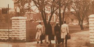 Four people walk past a Central State College sign onto the Wilberforce campus