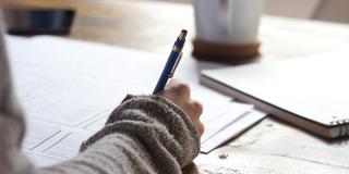 A person's arm holds a pen while taking a student course evaluation with a cup of coffee in the background