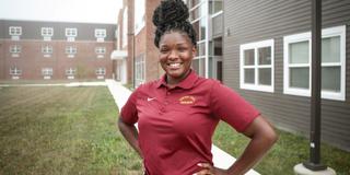 A young Black woman in maroon stands with hands on hips in front of residence halls at Central State University