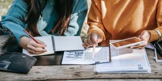 two students studying with notebooks and a mobile phone